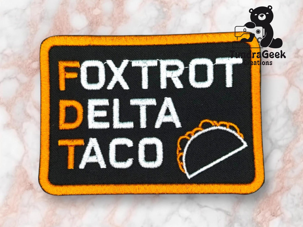 A rectangular patch with the words Foxtrot Delta Taco, the initials FDT, and a taco graphic, on a black background with an orange border.