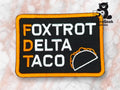 A rectangular patch with the words Foxtrot Delta Taco, the initials FDT, and a taco graphic, on a black background with an orange border.