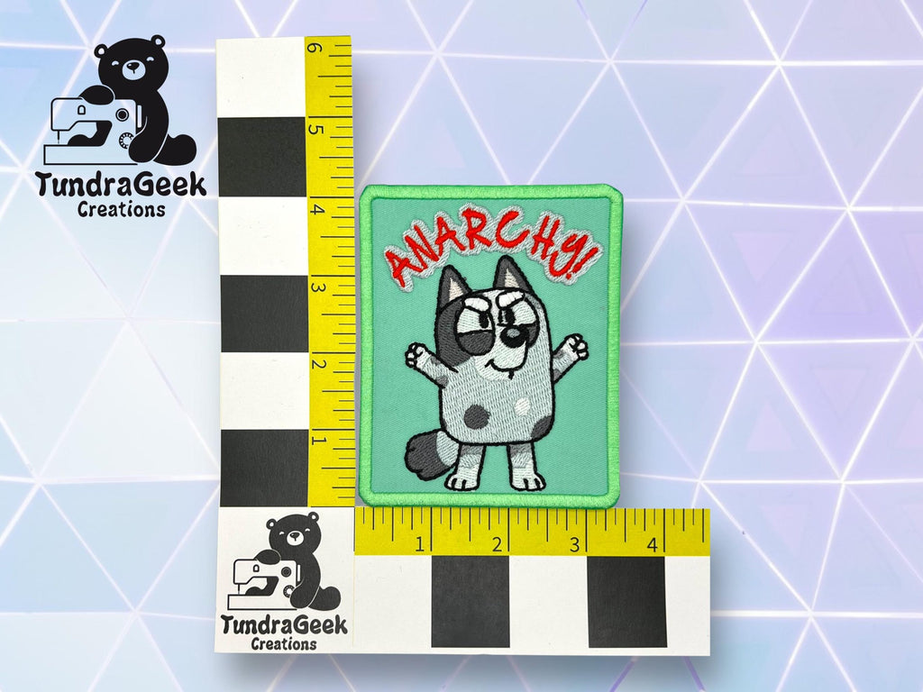 A rectangular embroidered patch with a cartoon dog, raised fist, and the word ANARCHY!! in red, shown with a measurement grid from TundraGeek Creations. Patch measures about 3x3 inches.