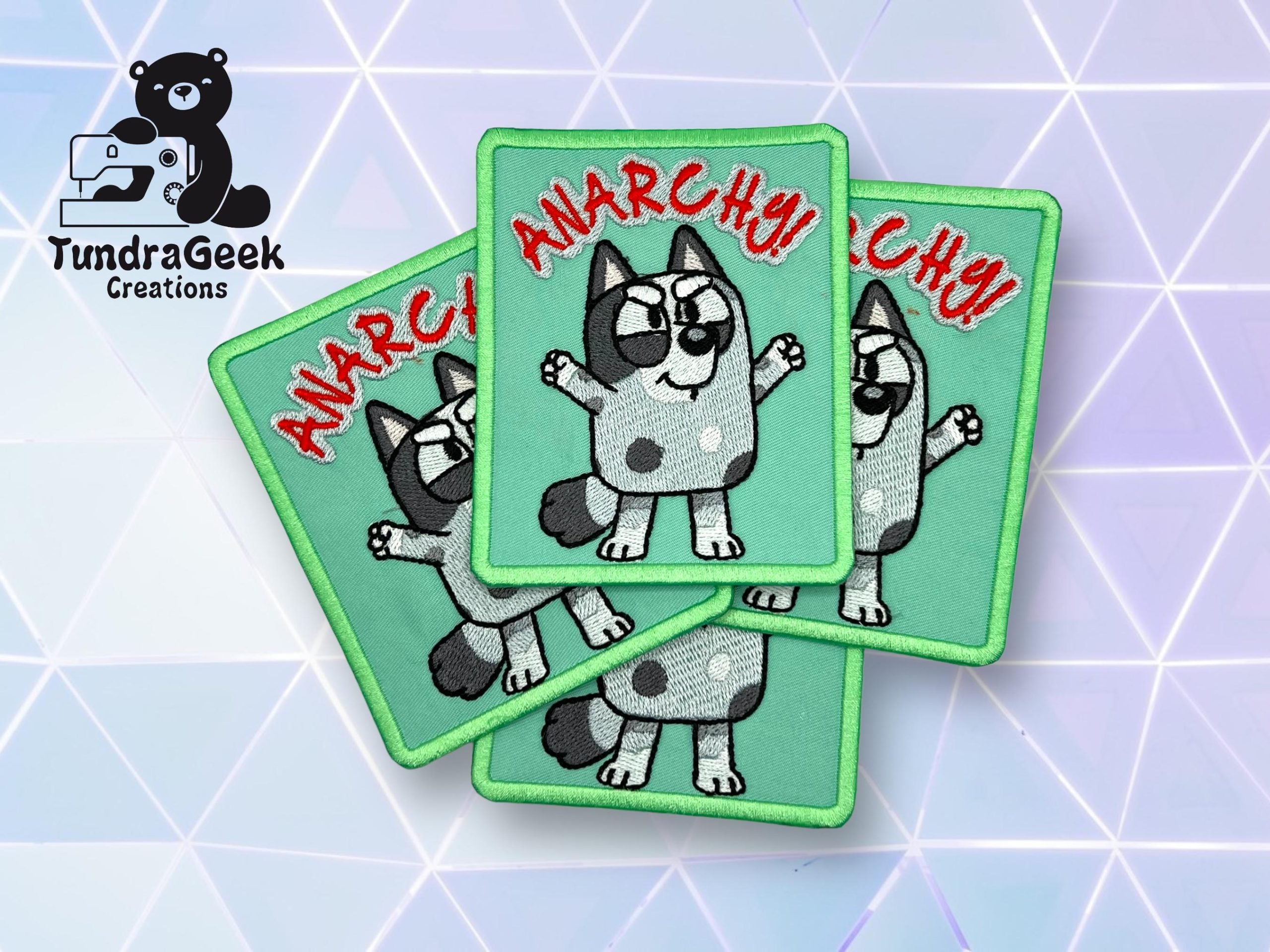 Four green embroidered patches with a cartoon dog, raised arms, sunglasses, and the word “ANARCHY!” in red. “TundraGeek Creations” logo is on the left. Geometric background.