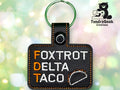 A black keychain with orange and white embroidered text reading Foxtrot Delta Taco, the letters F, D, and T in orange, and a small taco image; TundraGeek Creations logo in the corner.
