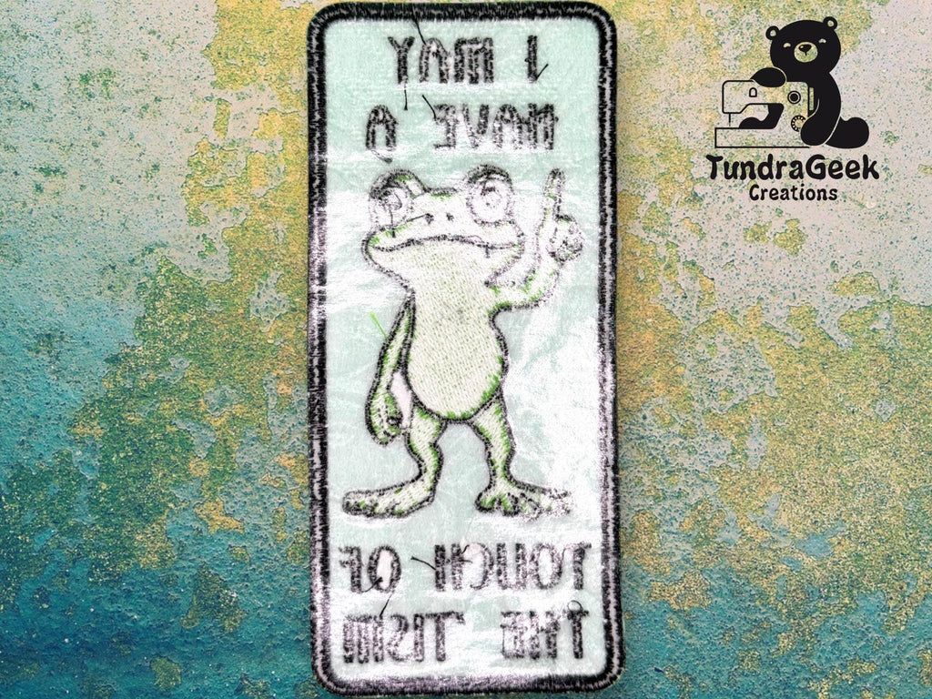 Rectangular patch with a cartoon frog holding up one finger. Text on patch is mirrored: I MAY HAVE 0 TOLERANCE FOR THIS. TundraGeek Creations logo in top right corner.