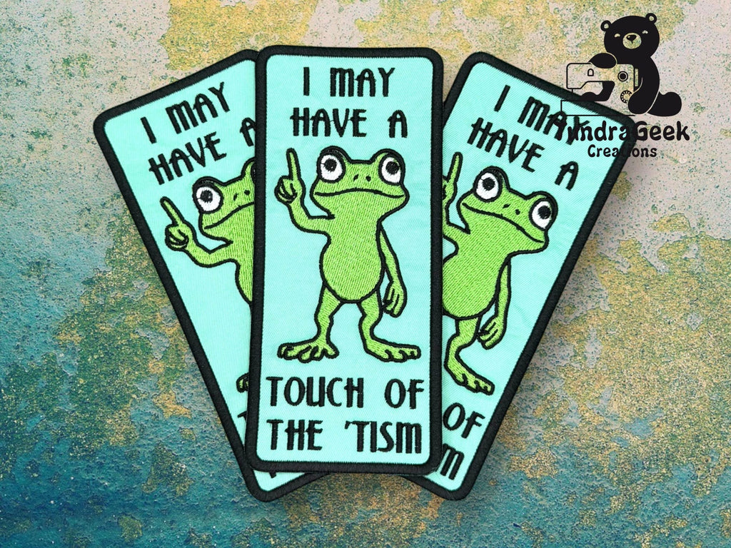 Three identical patches show a cartoon frog pointing upward with the text, I may have a touch of the tism. Background has a blue and green textured pattern.