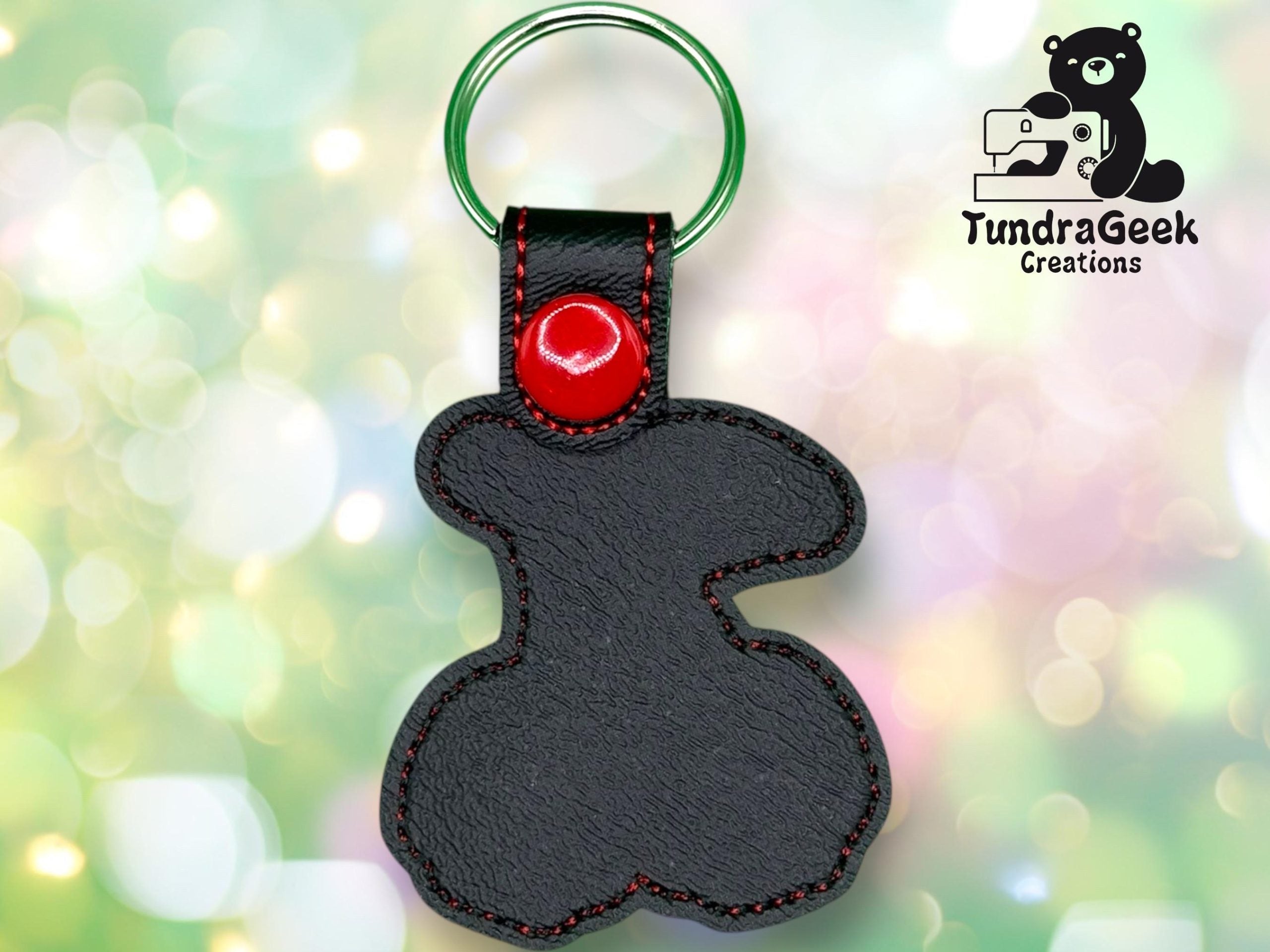 Black leather keychain with red stitching and button, shaped like a bear with a metal key ring. TundraGeek Creations logo featuring a bear and sewing machine in the top right corner.