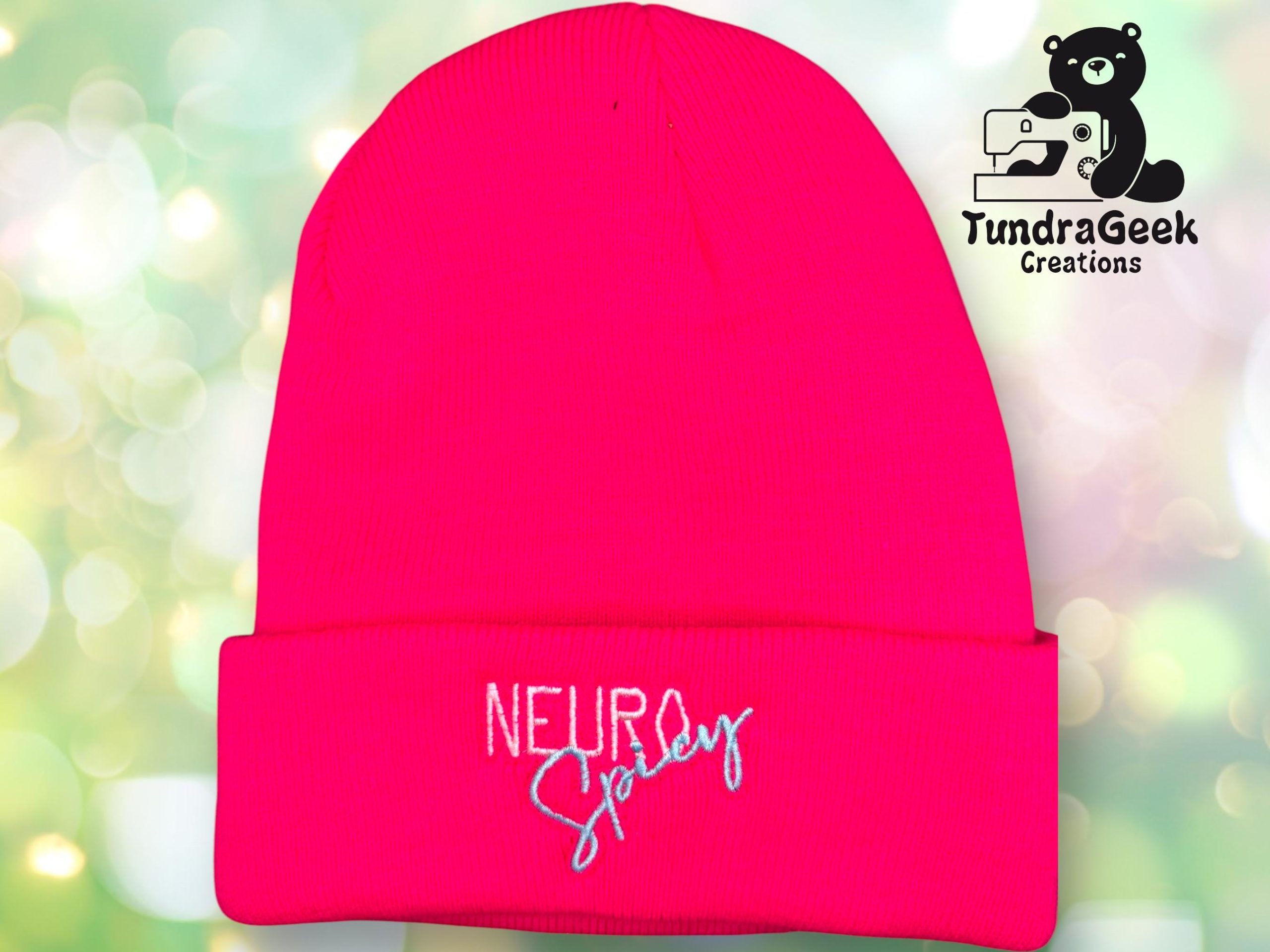 A bright pink beanie with the embroidered text NEURO Spicy on the front cuff. The TundraGeek Creations logo is in the top right corner.