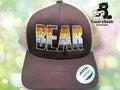 A trucker hat with the word BEAR embroidered in brown, orange, and white stripes, with a Snapback sticker on the brim and TundraGeek Creations logo in the background.
