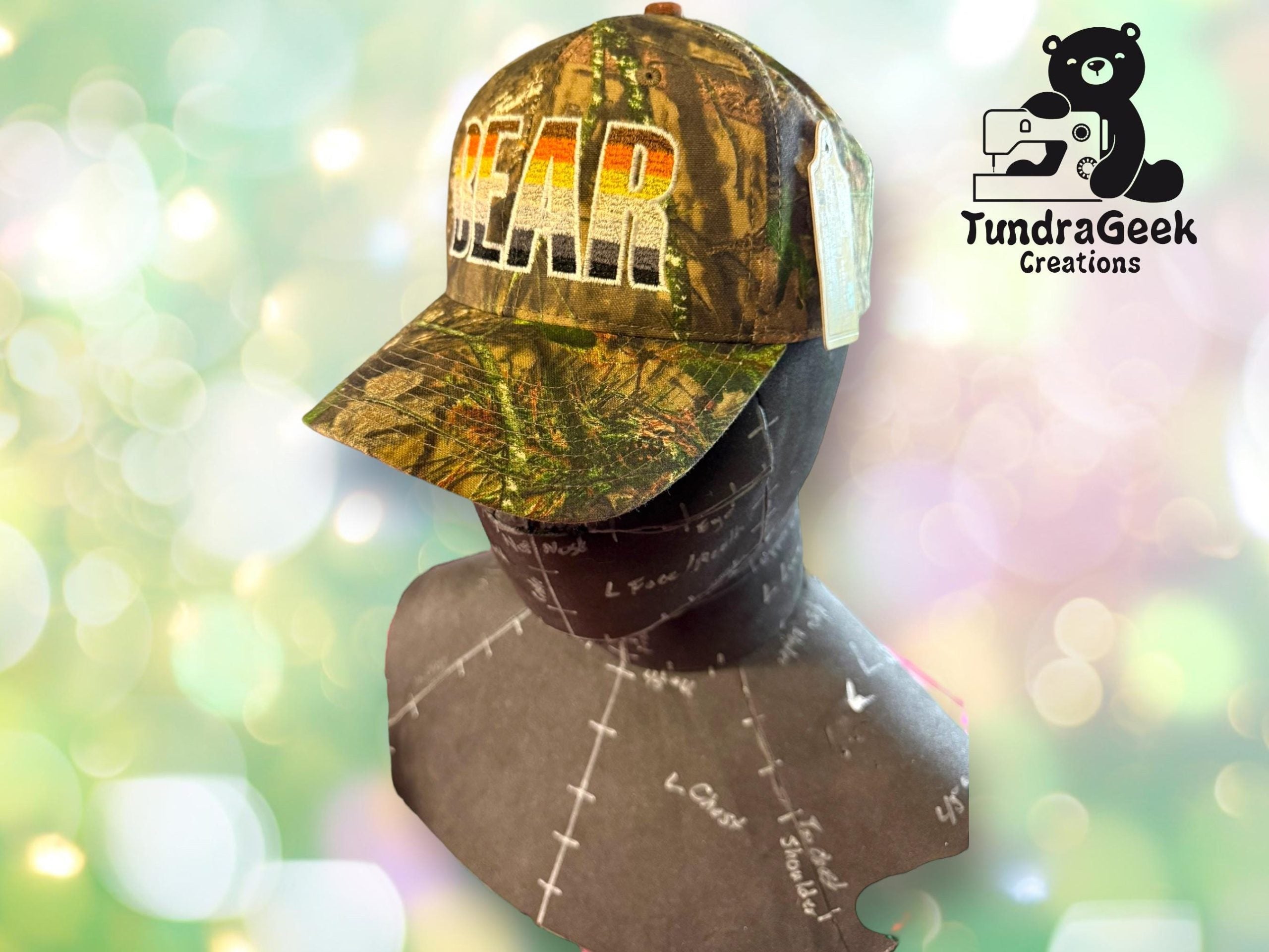 A camouflage baseball cap with BEAR in bold letters is displayed on a mannequin against a blurred background, with the TundraGeek Creations logo in the corner.