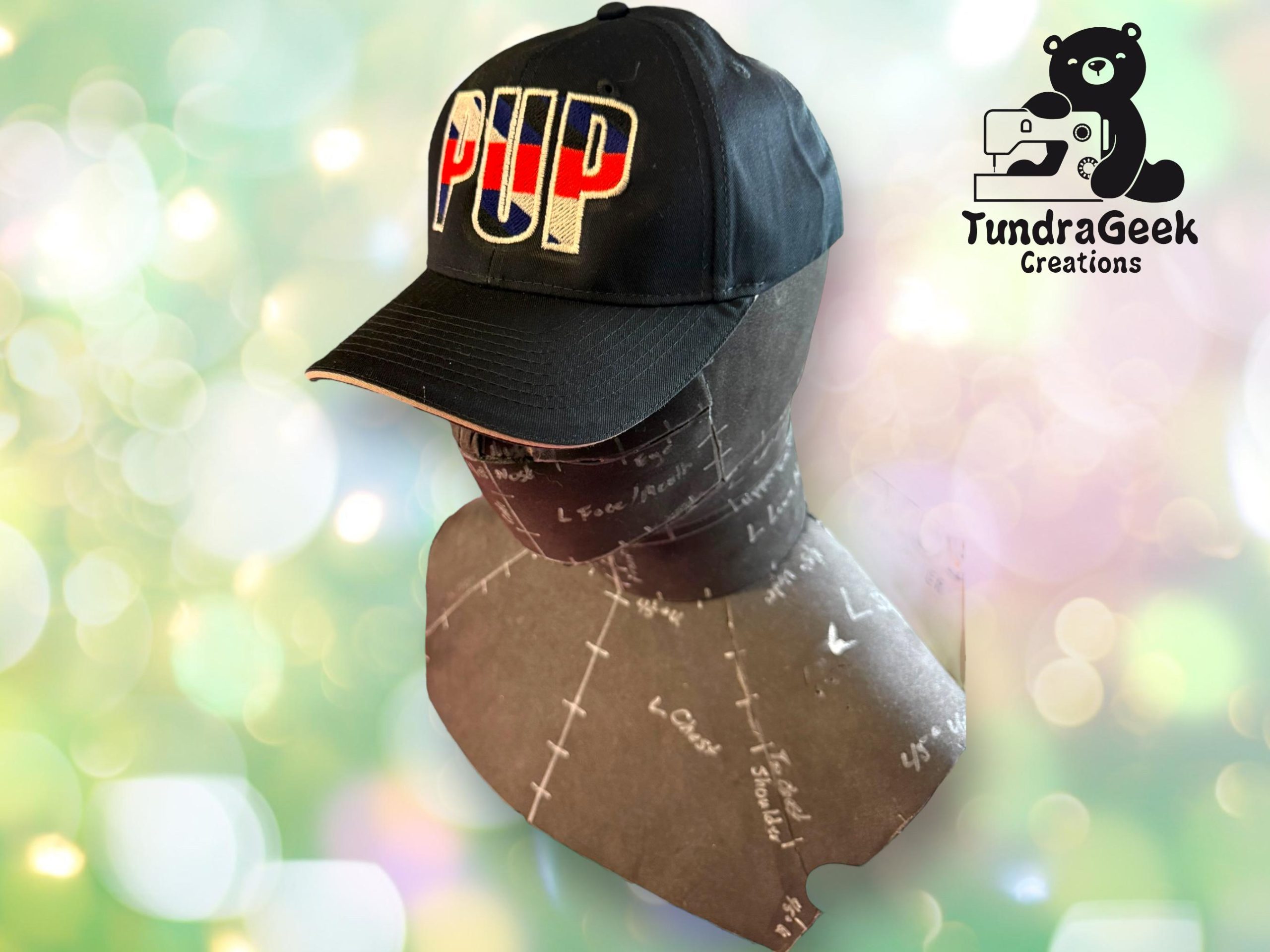 A black hat with PUP in block letters, featuring a red, white, and blue stripe, displayed on a mannequin head. TundraGeek Creations logo is in the top right corner.