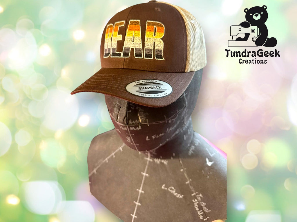 A mannequin displays a trucker hat with BEAR in bold letters. The TundraGeek Creations logo featuring a sewing bear is visible in the upper right corner.