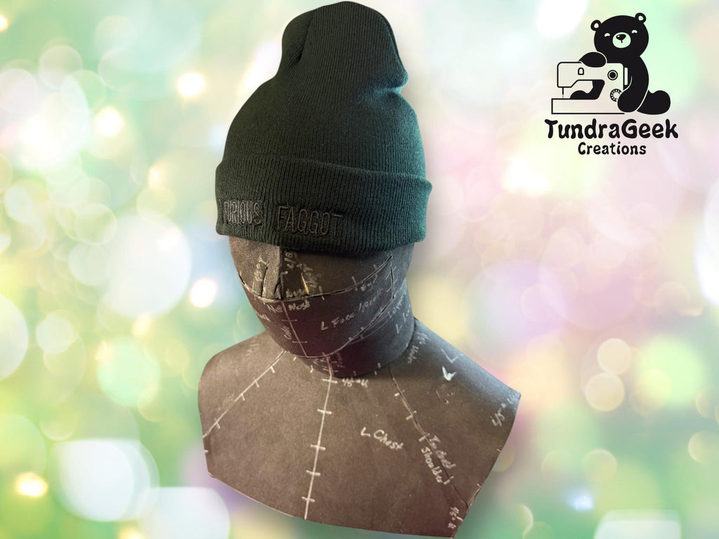 A mannequin head wearing a dark beanie with embroidered text, displayed in front of a light, bokeh background with the TundraGeek Creations logo in the corner.