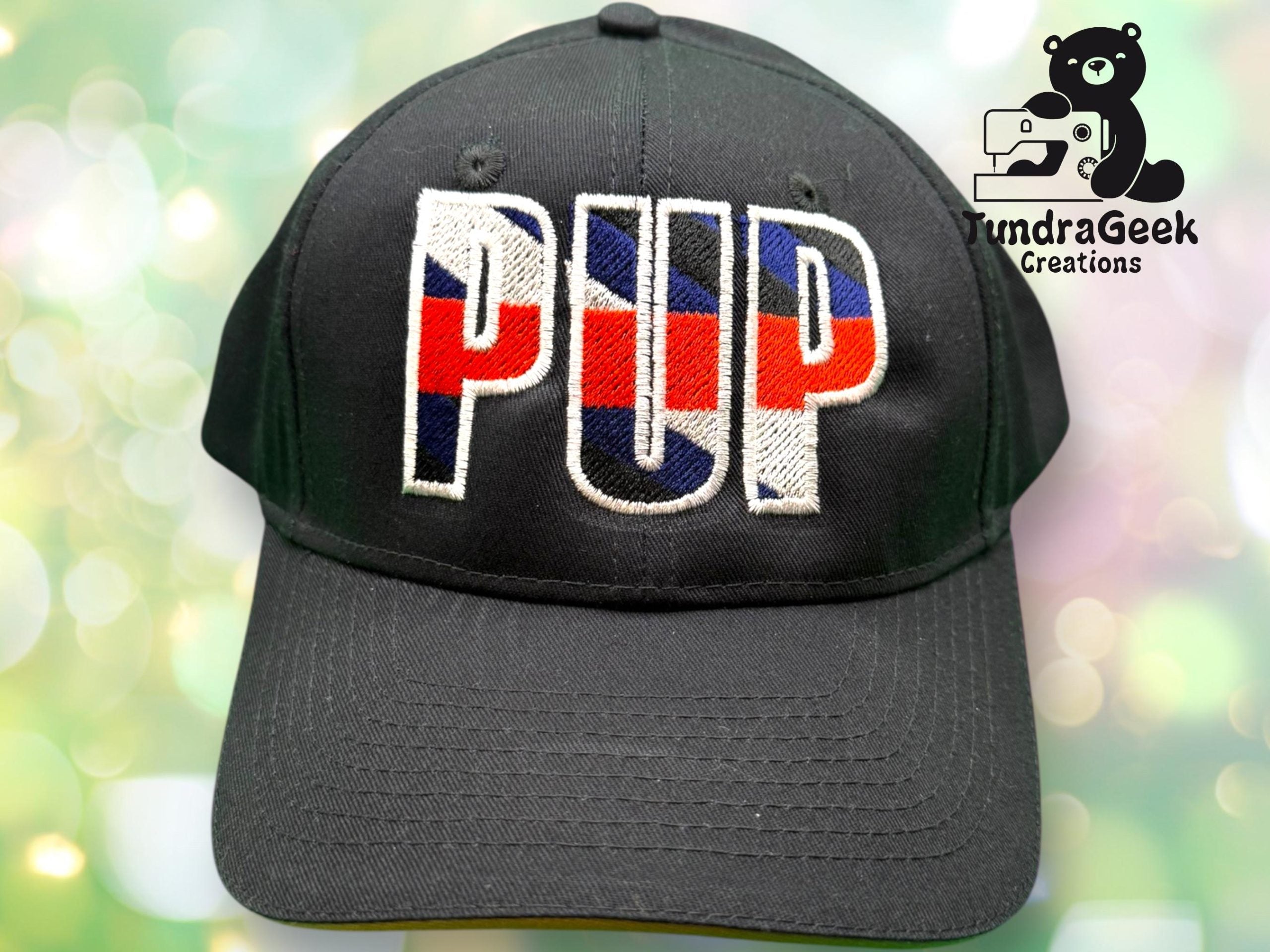 A black baseball cap with PUP embroidered in red, white, and blue letters; TundraGeek Creations logo featuring a bear and sewing machine in the background.
