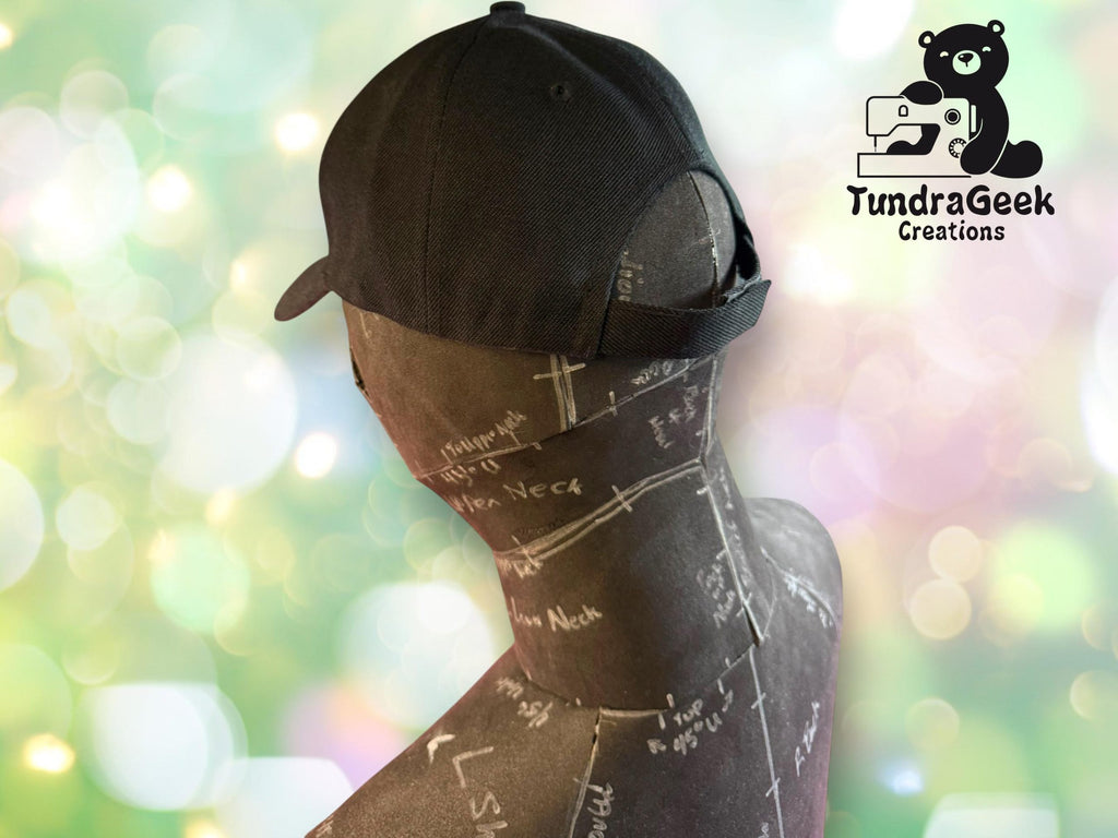 A black mannequin head wearing a black cap, with pattern markings visible; TundraGeek Creations logo appears in the upper right corner.