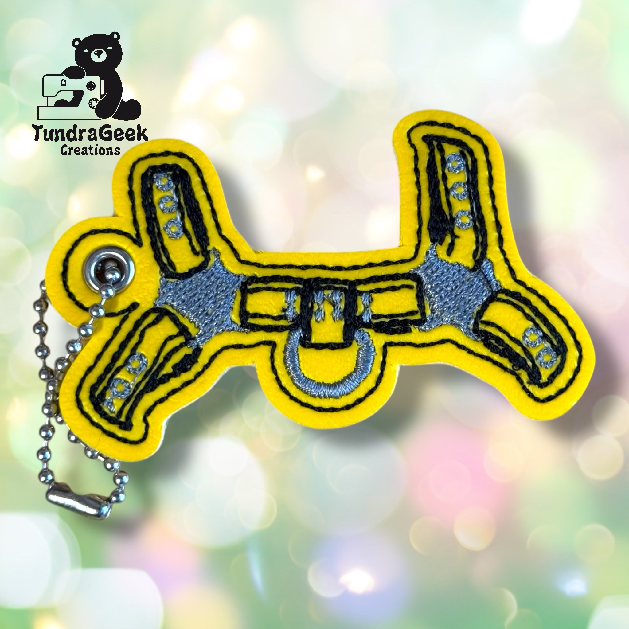 Yellow and gray embroidered keychain shaped like a Star Wars Mandalorian jetpack, with a metal ball chain and the TundraGeek Creations logo in the background.