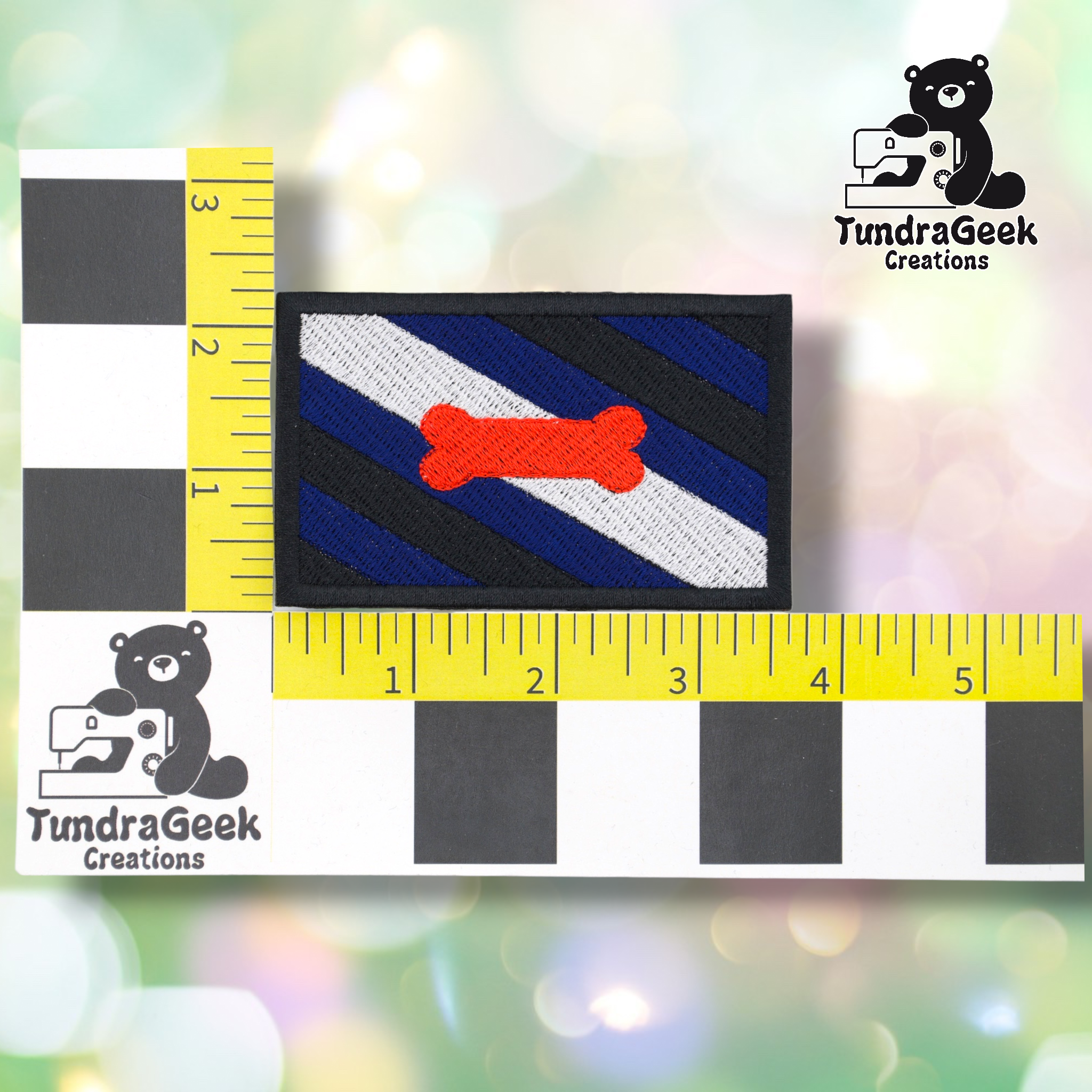 The Pup Pride Flag Patch features diagonal black and blue stripes, a white stripe, and a red bone, shown on a measurement grid with TundraGeek Creations logos. Perfect embroidered sew-on or iron-on patch for pup play gear!.